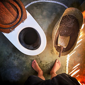 The feet of a man standing in front of an eco-friendly dry toilet.