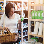 A woman is grocery shopping and reading product information on a label.