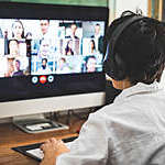 Back view of woman with headphones joining in a video conference from home.