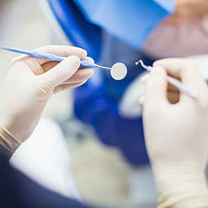 Close up of the hands of a dentist with surgical gloves and tools in hand.