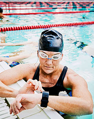 Female swimmer checks her fitness watch during exercise in an outdoor pool.