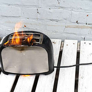 Black and steel toaster with two slices of toast catches fire.