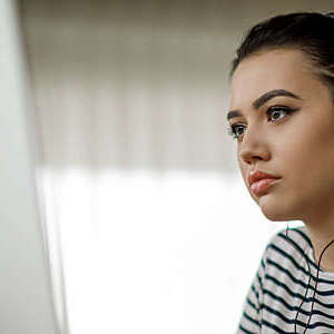 Young woman with headphones looks absorbed as she participates in a distance-learning course.