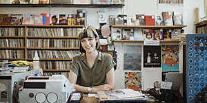 Portrait of a female retail worker standing behind the counter in a record store, smiling at camera.