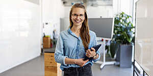 Portrait of a businesswoman with eyeglasses standing in office. Female entrepreneur looking at camera and smiling holding a digital tablet.