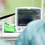 Cardiogram monitor in surgery while not recognisible doctor operates, focus on screen