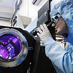 Female scientist in protective clothing and goggles uses a purple beam laser equipment.